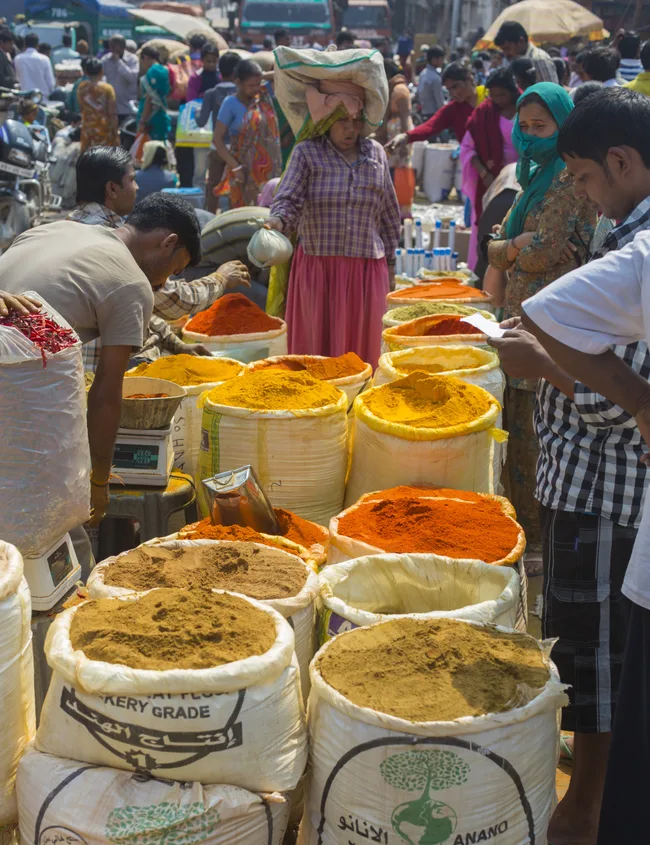 Market scene with people buying spices in large sacks, including turmeric and chili powder, vibrant and colorful.
