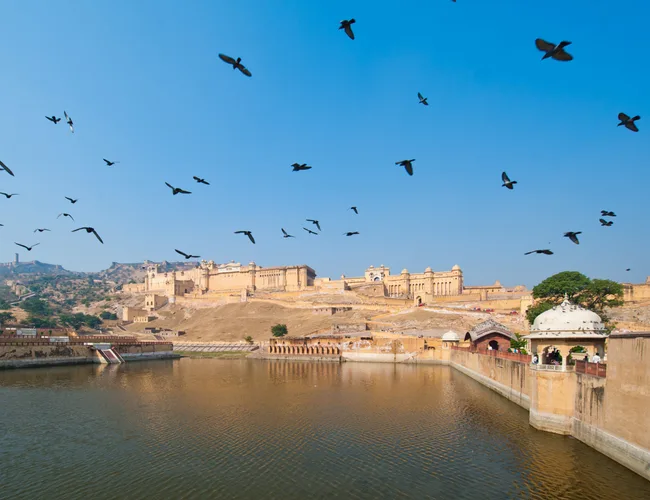 Amber Fort in Jaipur, India, with birds flying over the water on a clear day.