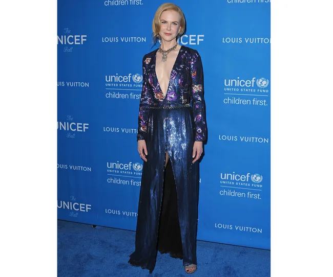 A person in a deep V-neck sequin gown poses at the UNICEF Ball with a blue backdrop displaying logos.