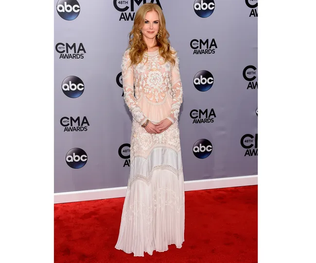 A woman in a long white lace dress at the 48th CMA Awards, standing on the red carpet in front of an event backdrop.