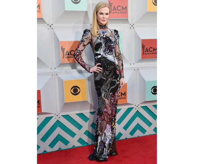 Elegant woman in a patterned, long-sleeve gown stands on red carpet at an awards event.