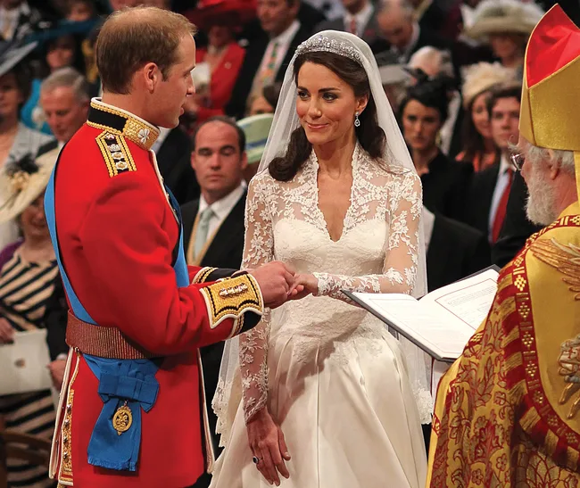 A couple exchanging rings at a wedding ceremony, with guests observing in the background.