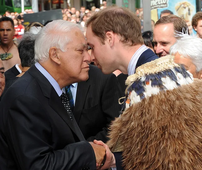 Two men greet with a traditional Maori hongi, touching noses, in a crowded outdoor setting.