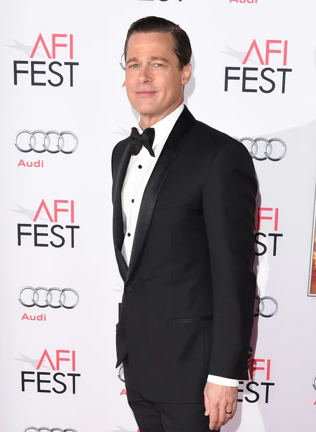 A man in a black tuxedo poses at the AFI Fest event with logos in the background.