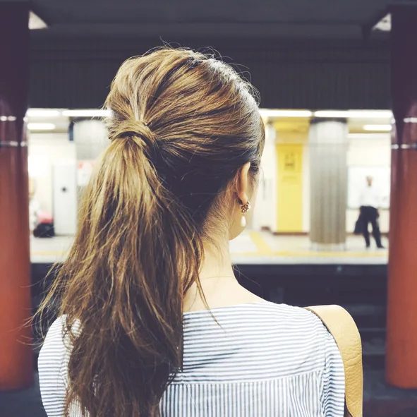 Rear view of a woman with a ponytail at a subway station, wearing a striped shirt.