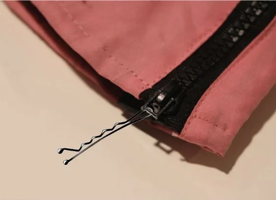Pink fabric with a black zipper partially closed using a bobby pin as a makeshift zipper pull.