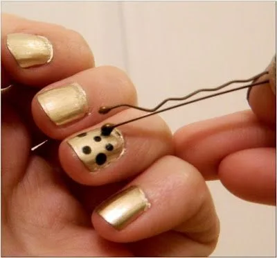 Hand painting black dots on gold nails using a bobby pin for nail art.
