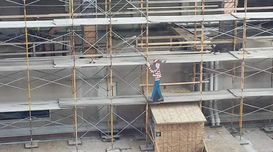 Cardboard cutout of Waldo on a construction scaffolding, wearing a red and white striped shirt and blue pants.