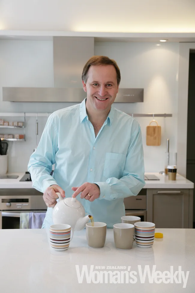 Man in light shirt pouring tea into mugs in a modern kitchen, smiling at the camera. "New Zealand Woman's Weekly" text visible.