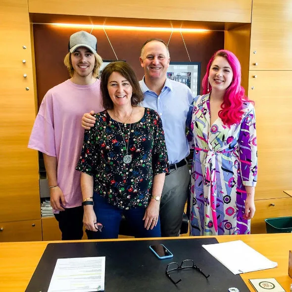 Four people smiling and standing together in an office setting, with a desk in front of them.
