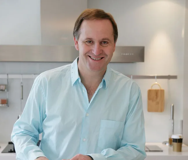 Man smiling in a kitchen wearing a light blue shirt.