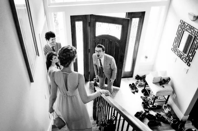 Four people at a front door, one on stairs, with shoes scattered around the entryway, in black and white.