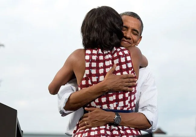 Man and woman embracing warmly, with the man smiling and wearing a white shirt and watch, and the woman in a patterned dress.