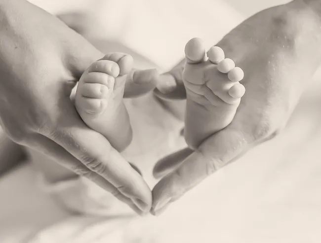 Adult hands gently hold a baby's tiny feet, forming a heart shape.