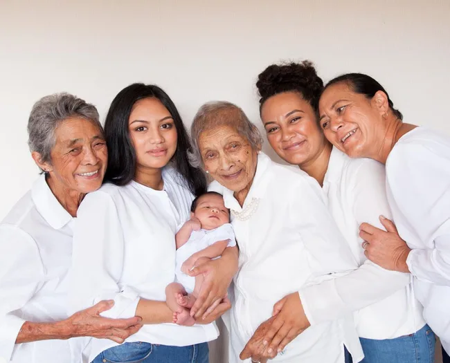 "Five generations of women posing together, dressed in white, with a baby cradled by the oldest woman."