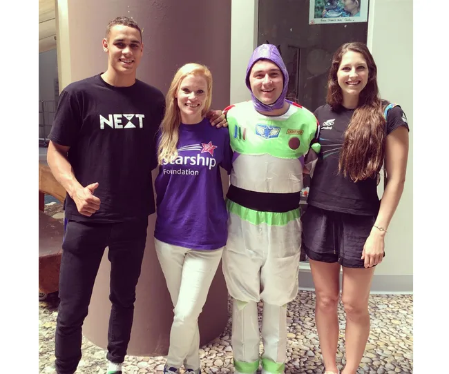 Four people, one in a Buzz Lightyear costume, smiling and posing together indoors.