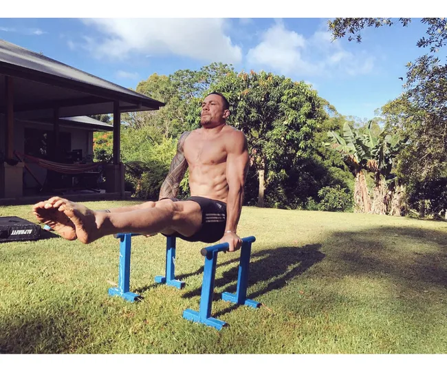 Man performing L-sit exercise on parallel bars in a garden.