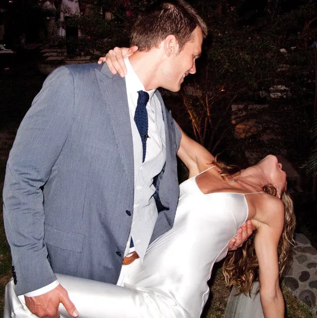 Man in a blue suit romantically dips a woman in a white dress at an evening event.