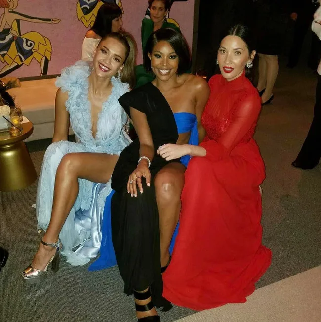 Three women in elegant dresses sitting together, smiling at a formal event.