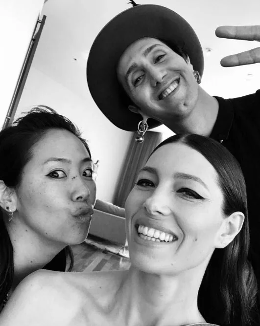 Three people smiling in a black and white selfie; one wears a hat, another puckers lips, and a third has long hair.