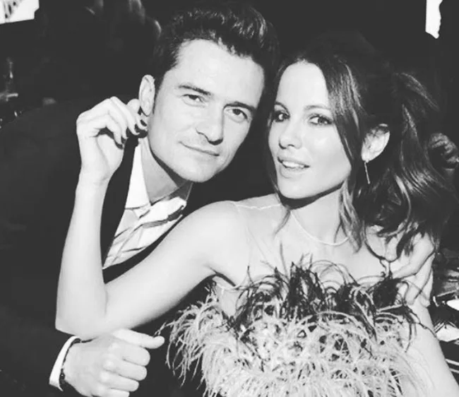 Two people pose closely together, one dressed in a suit, the other in a feathered outfit, black and white photo.