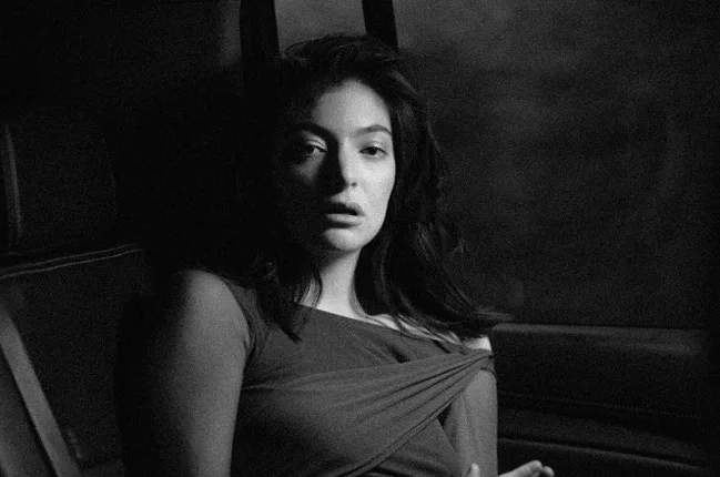 Grainy black and white portrait of a woman seated in a car, looking towards the camera.