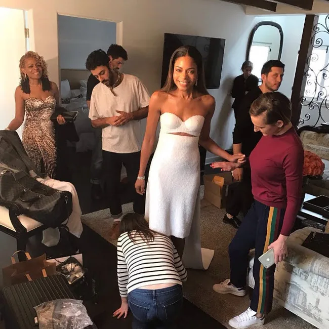 Alt text: Woman in white dress with group in a room preparing for an event.