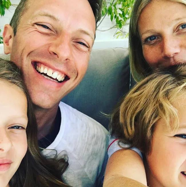 Four people smiling closely together, including two adults and two children.