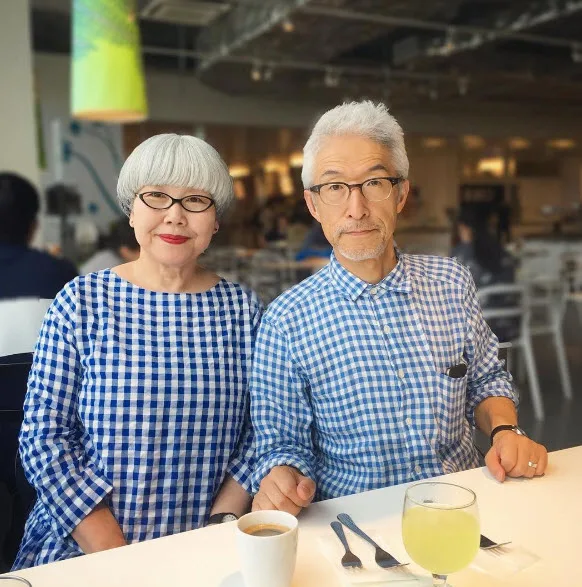 Elderly couple in matching blue checkered outfits sitting at a table with drinks in a cafe.