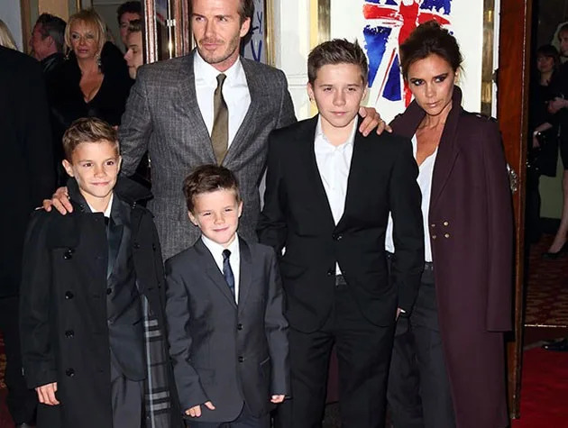 A well-dressed family poses together on a red carpet event, with formal attire and a backdrop featuring a Union Jack.