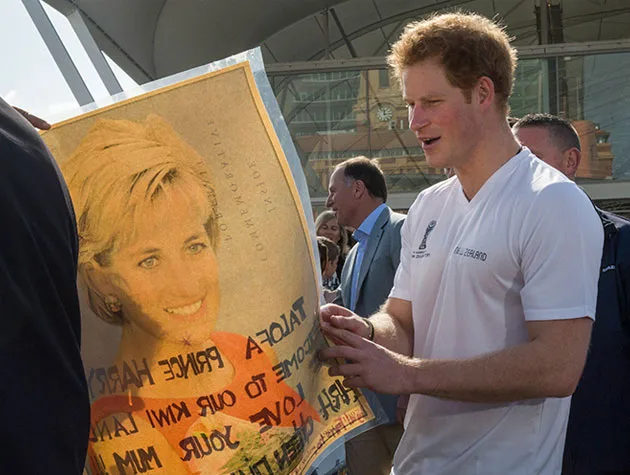 Man holding a poster with Princess Diana's image, outdoors under a modern structure, with people in the background.