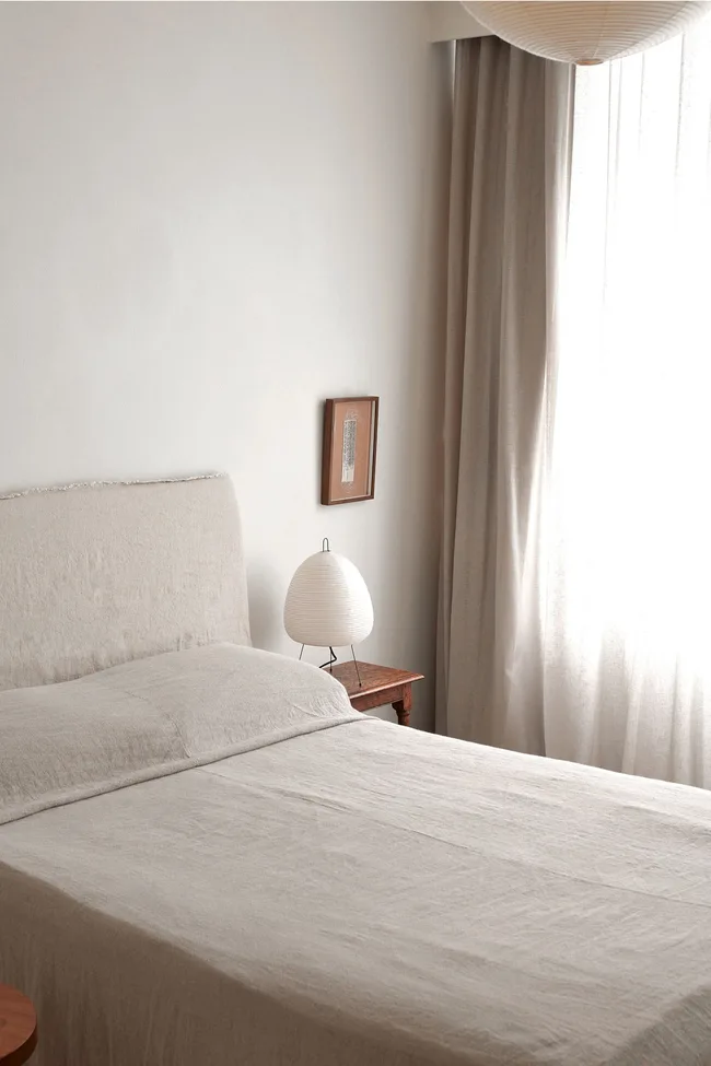 A neutral bedroom with linen bedding and a lantern on the bedside table