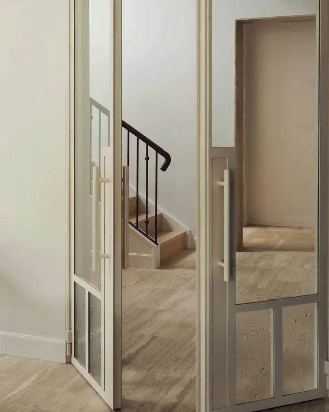 Vein-cut Travertino Vallanca from Bisanna Tiles lines the entry. Doors in powdercoated steel.