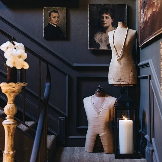 A painted black stairwell with mannequins and portraits inside Susie Anderson Home, a shop in the Southern Highlands, Australia