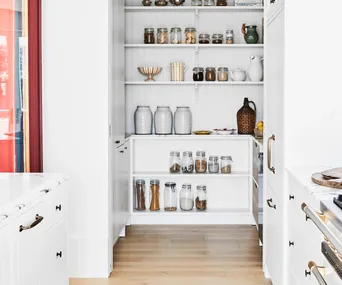 A white kitchen with an open pantry filled with neatly-stored dried goods