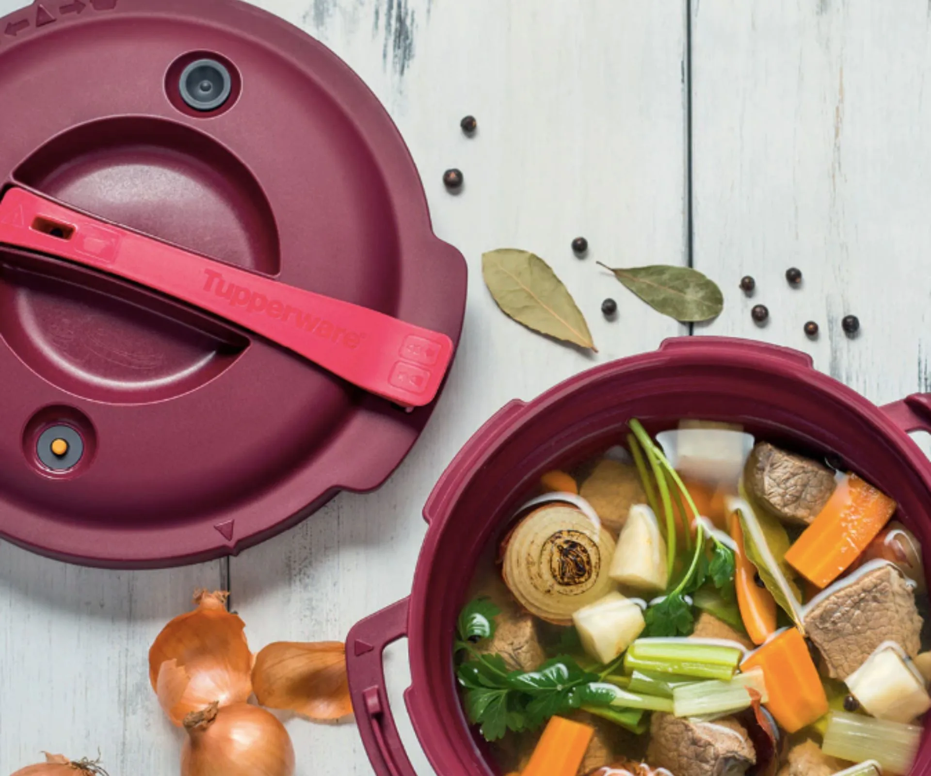 red pressure cooker filled with vegetables on a white wooden background