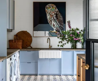 A stylish blue laundry with antique tiles and a large owl painting hanging above a country sink