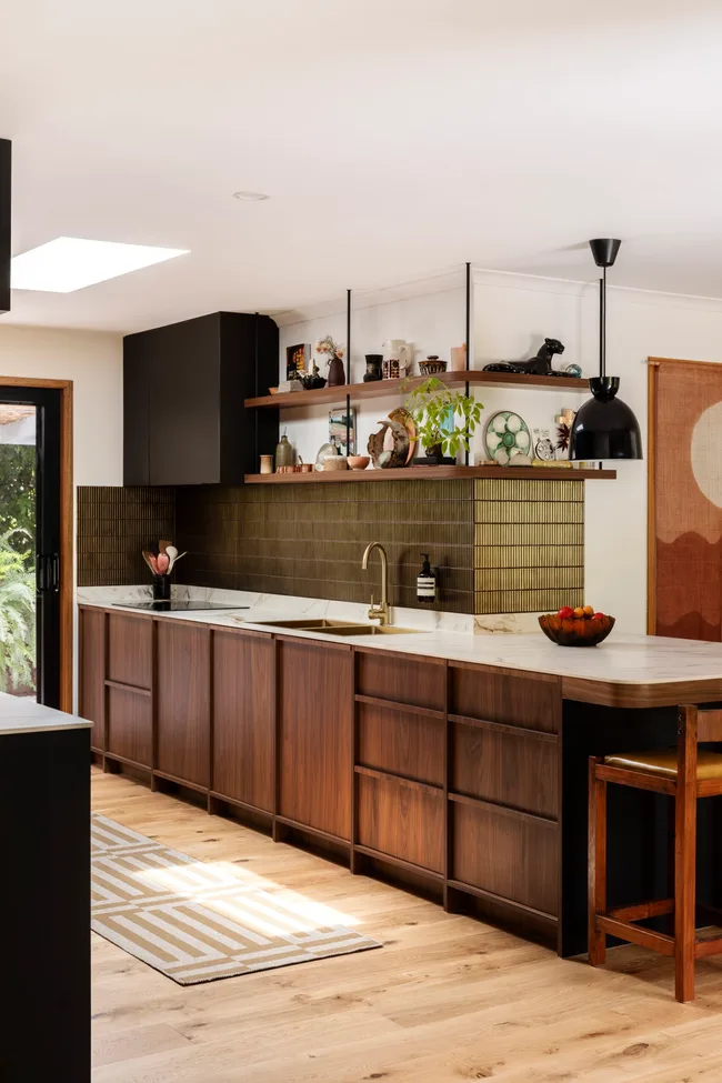 A renovated kitchen with dark timber cabinetry, green-gold tiling and marble benchtops