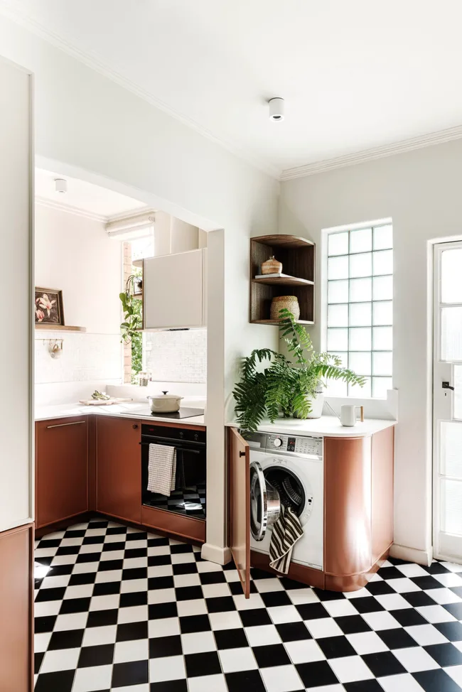 A kitchen with checkerboard tiling and burgundy cabinetry