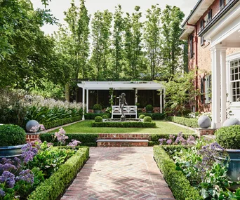 A manicured garden with brick paving outside a Georgian-style home