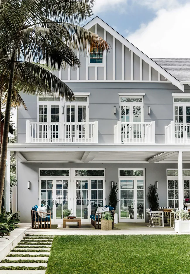 The exterior of a Hamptons-style double story home with a large green lawn and palm trees