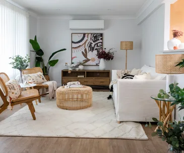 Cozy living room with wicker furniture, white sofa, and decorative plants, featuring a stylish abstract wall art piece.