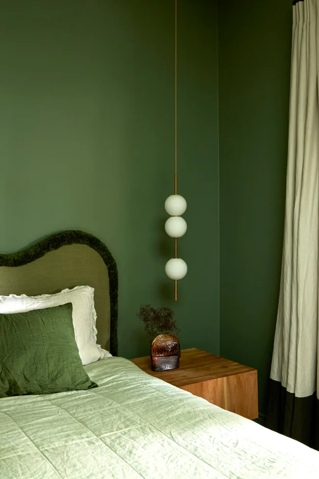 A green colour drenched bedroom with a pendant light and curved green headboard