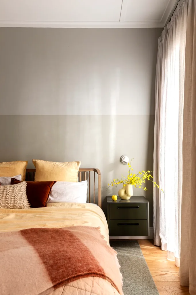 A bedroom with a two tone wall and pastel yellow bedding