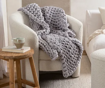 A chunky knit-style weighted blanket on a boucle armchair