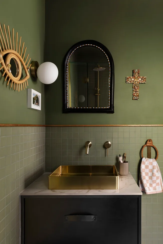 A green bathroom with a gold metal sink and hanging art