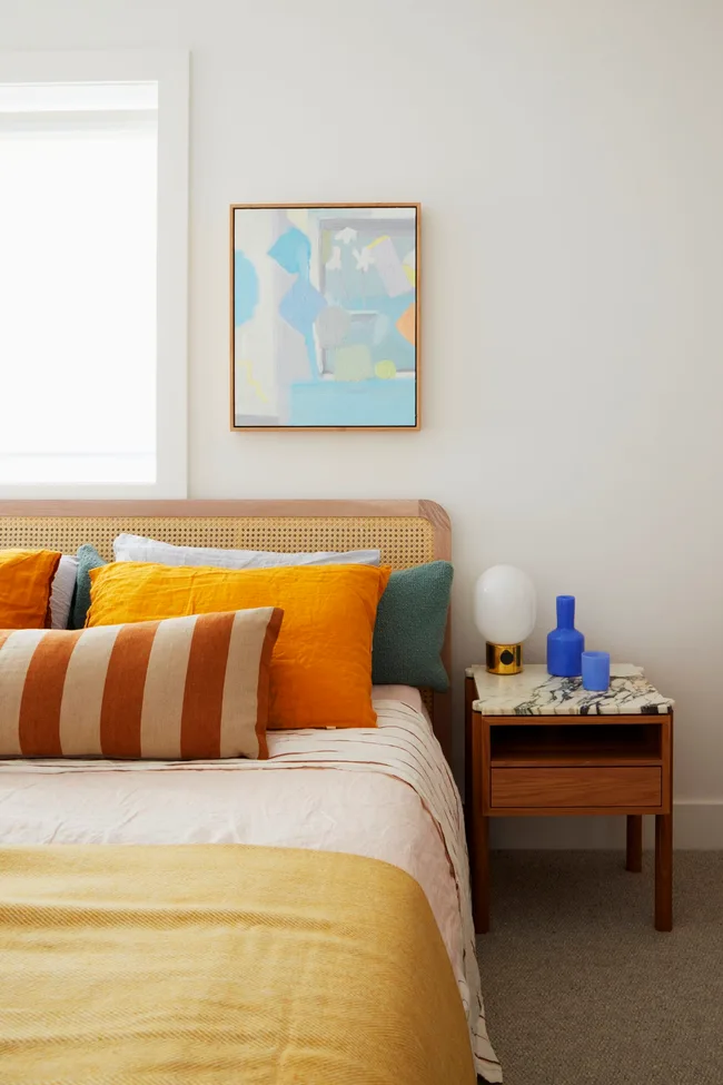 A white bedroom styled with colourful bedding and a marble and timber bedside table