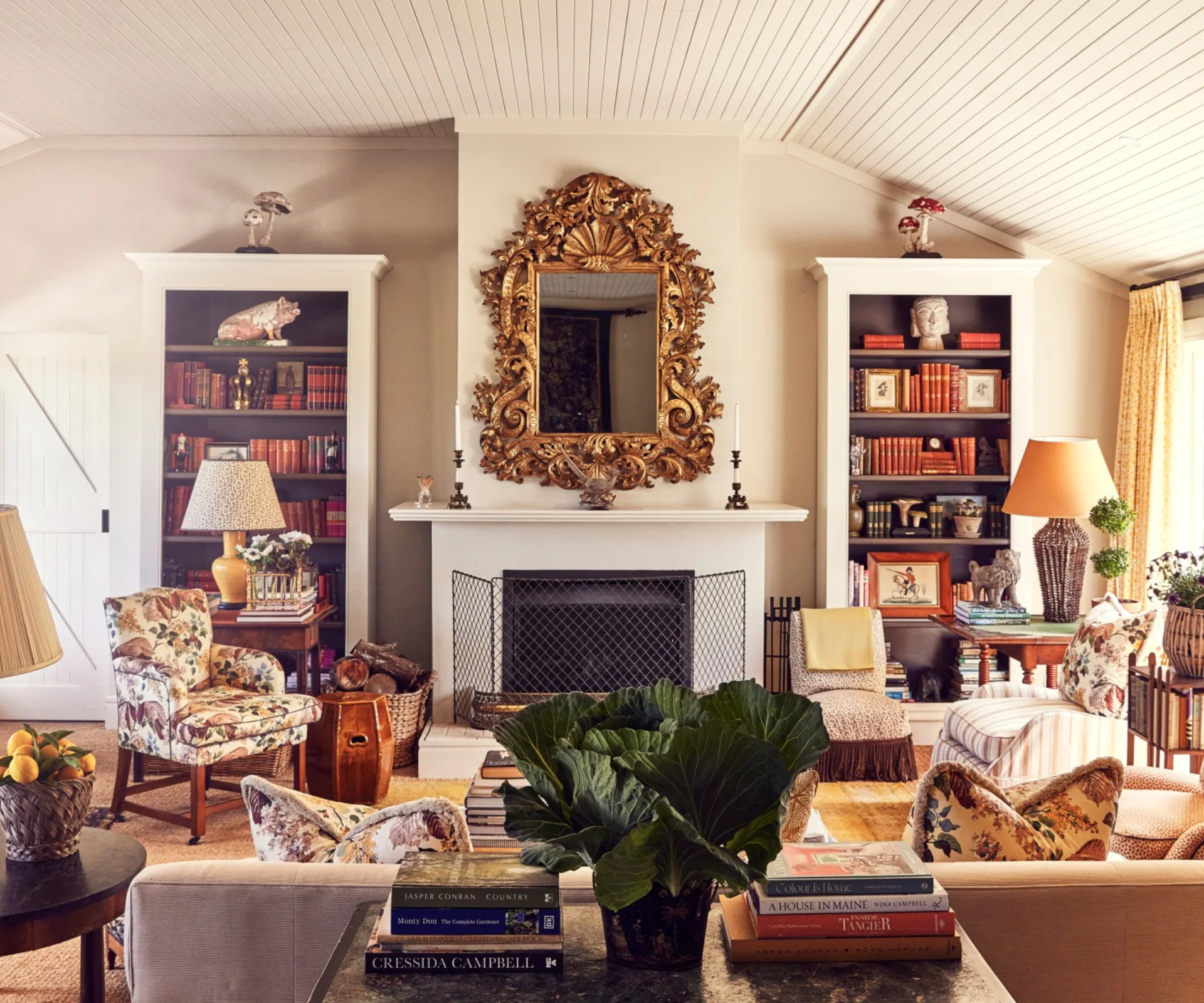 A large colourful and cosy living area centred around a fireplace with a gilded mirror hanging above