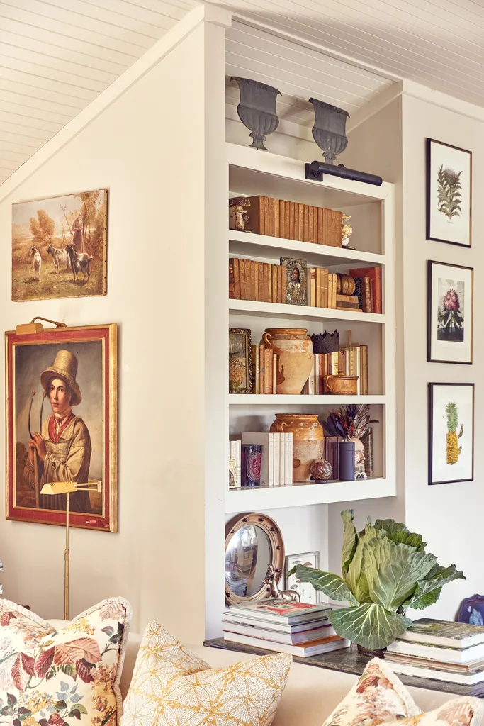 A bookshelf filled with books and old pottery and a wall covered in framed art prints