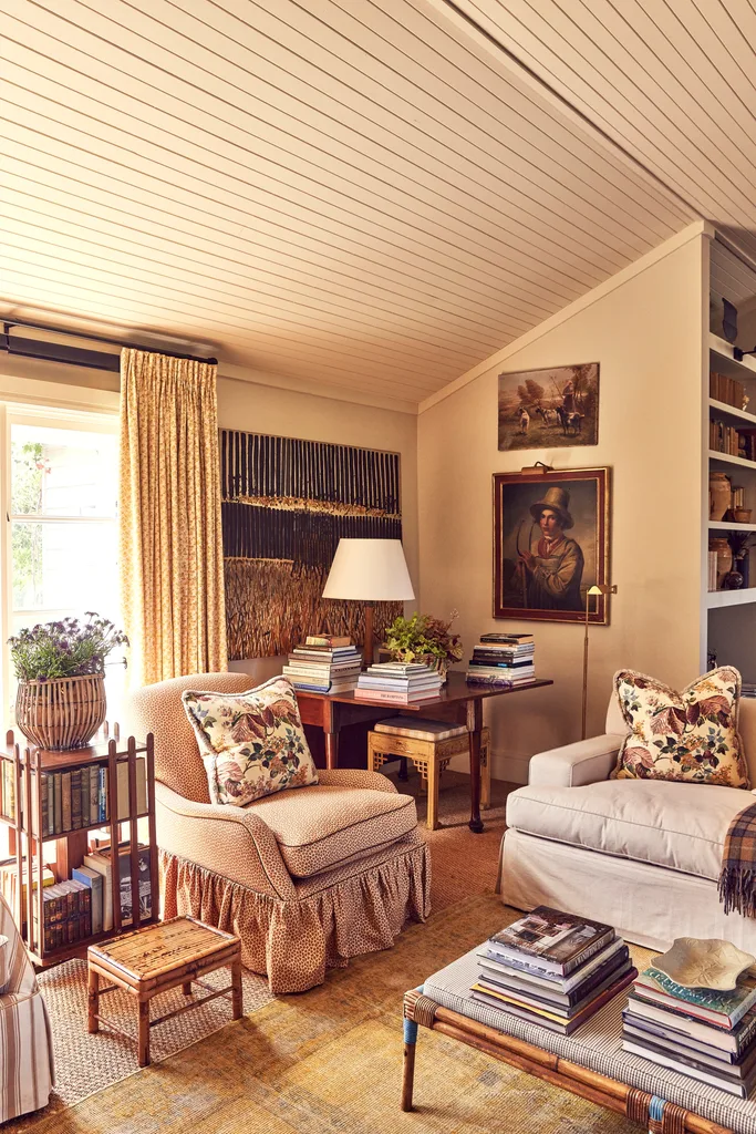 A country-style living area with a skirted armchair and coffee tables covered in books